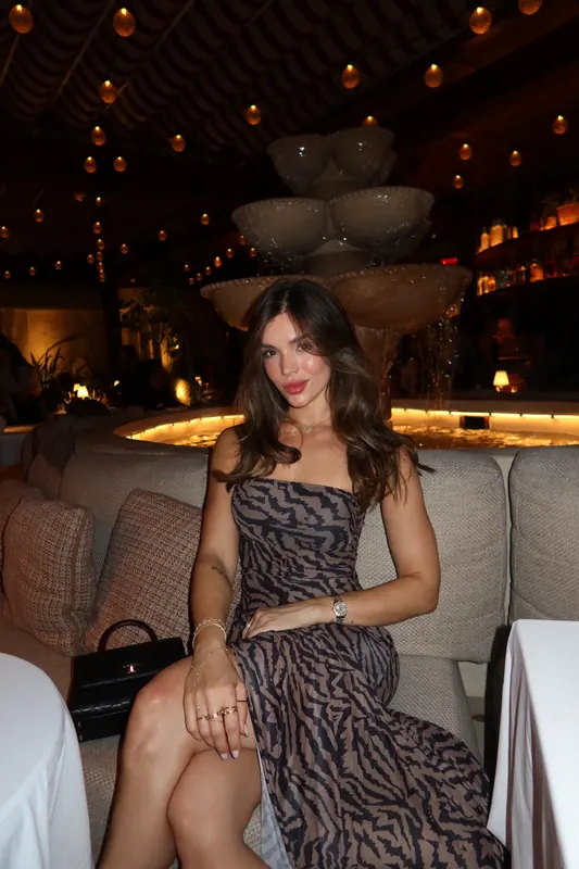 Gabryelle Pedroso seated in an animal-print evening dress under warm restaurant lighting