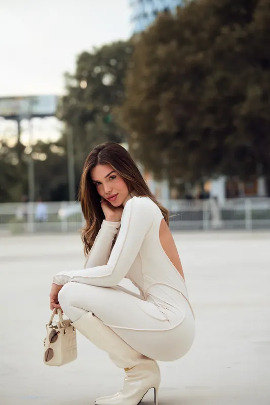Gabryelle Pedroso posing outdoors in a fitted white jumpsuit and white boots